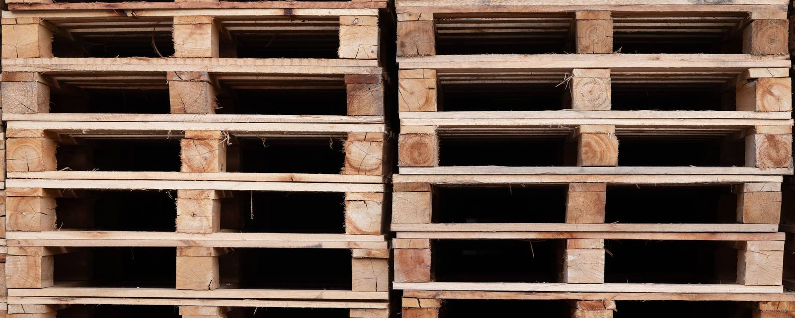 Close view of two tall stacks of used wooden pallets, seen from the end