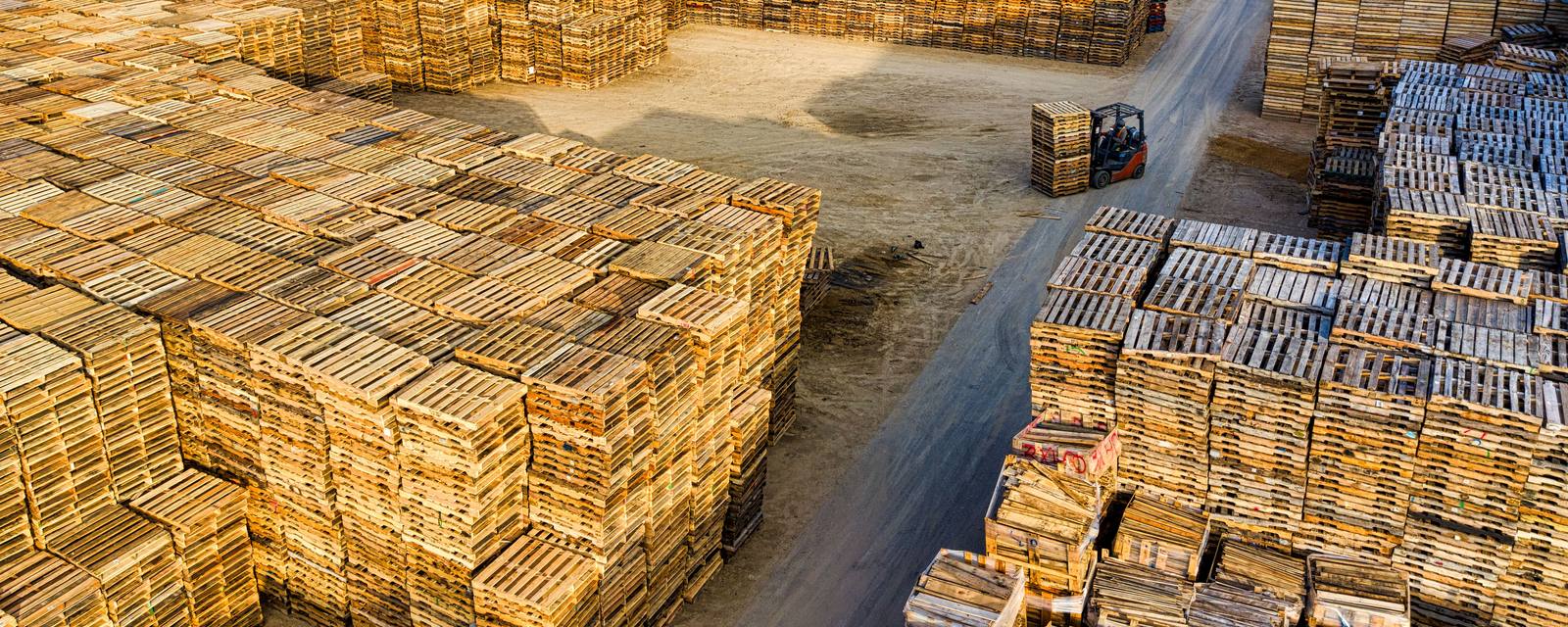Aerial view of a pallet yard with a forklift working between big stacks of wooden pallets